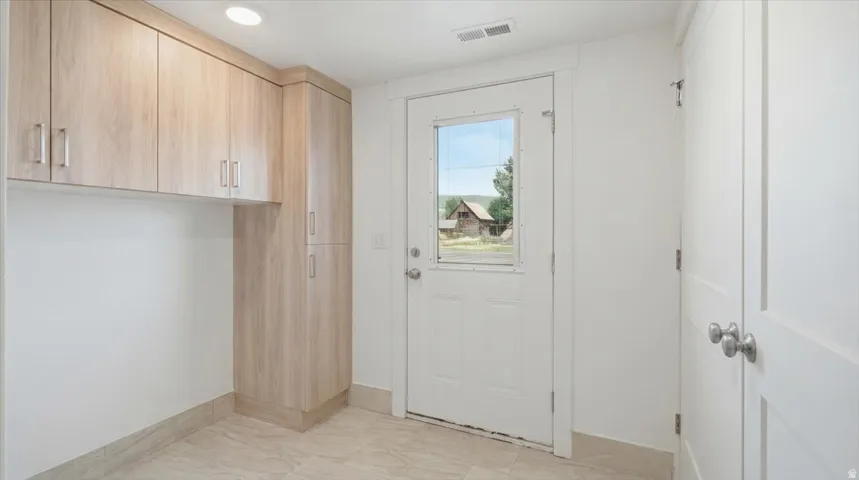 Entryway featuring light wood-finish cabinetry with brushed nickel hardware, white paneled doors, and square tile flooring