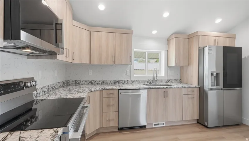 Modern kitchen featuring light wood-finish cabinetry, granite-style countertops, stainless steel appliances, and wood-finish flooring