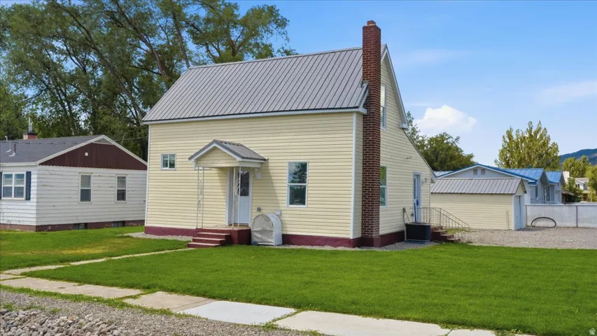 Two-story residence featuring light yellow siding, a metal roof, and a prominent brick chimney