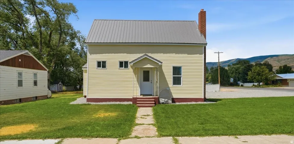 Light yellow siding exterior with a metal roof and a brick chimney