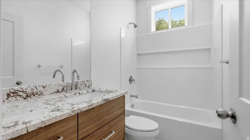 Bathroom featuring a wood-finish vanity with a stone countertop, an integrated sink, and dual chrome faucets
