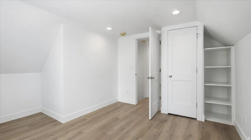 Room featuring wood-finish flooring, recessed lighting, white walls, built-in shelving, and white two-panel doors