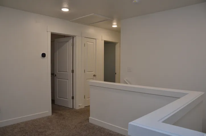 Upper-level landing featuring plush gray carpeting, white painted walls, recessed lighting, and white trimmed doorways