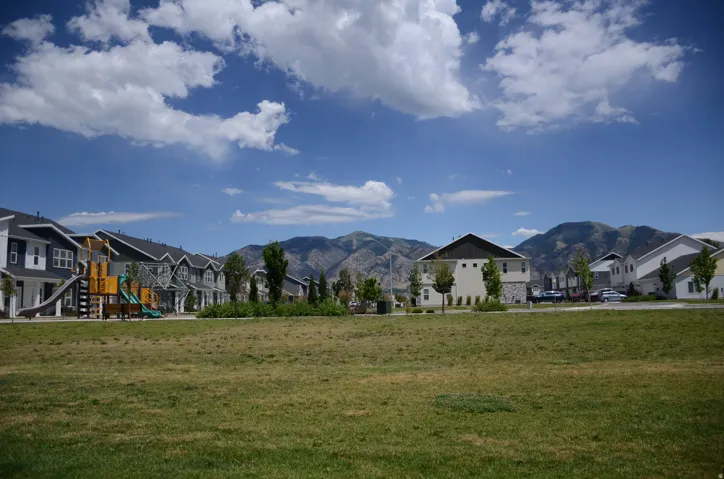 Expansive green space with mature landscaping, surrounded by multi-story residential buildings featuring varied siding materials and dark-toned roofs