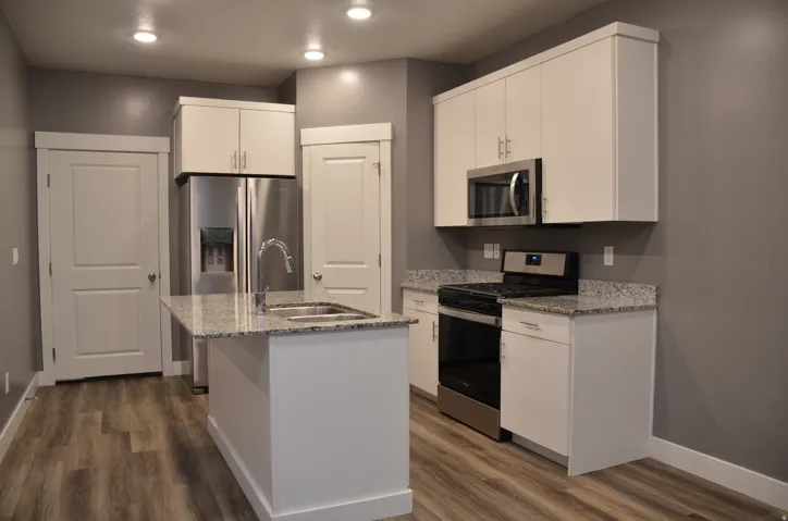 Kitchen featuring white shaker cabinetry, stainless steel appliances, speckled granite countertops, a central island with an undermount sink, and wood-finish flooring