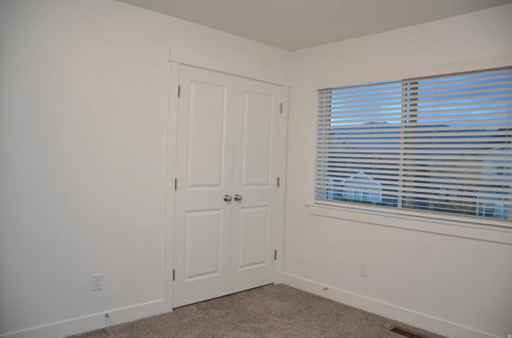 Bright room featuring a double-door closet with polished chrome hardware, a window with horizontal blinds, and neutral carpeting