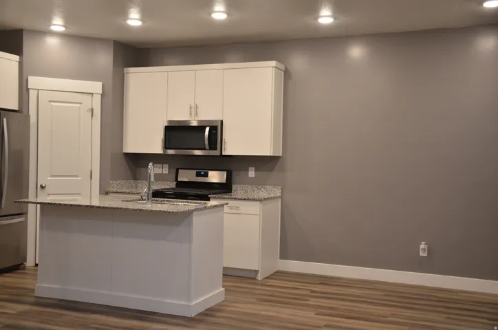 Modern kitchen featuring an island with an integrated sink, white cabinetry, speckled countertops, and stainless steel appliances