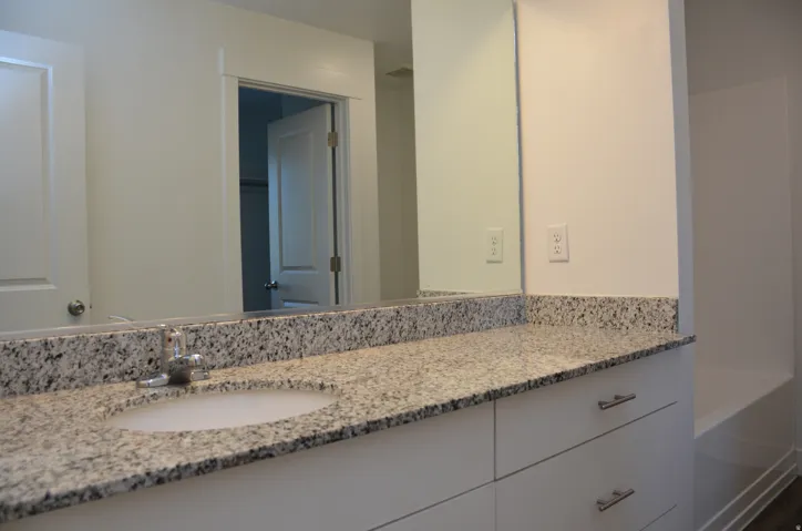 Granite-finish countertop with an undermount sink, chrome faucet, white cabinetry, and a full-width mirror