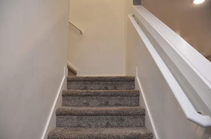 Carpeted staircase featuring a painted handrail and white baseboards