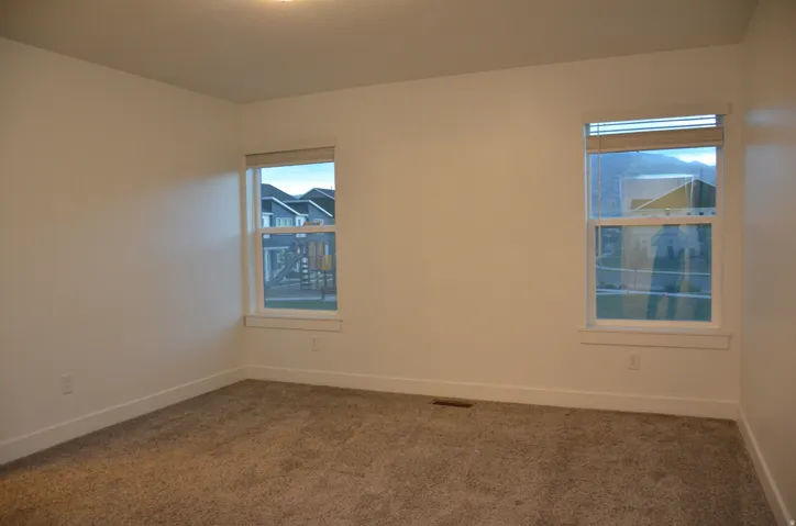 Bright interior space featuring two windows with blinds, plush carpeting, and clean white walls