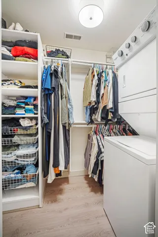 Laundry closet featuring a stacked washer and dryer, wood-finish flooring, built-in shelving, and hanging rod storage