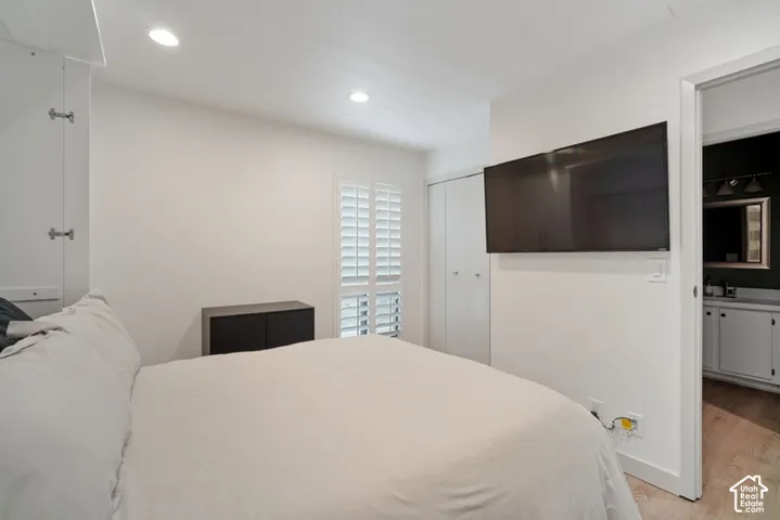 Bedroom featuring recessed lighting, plantation shutters, and light wood-finish flooring extending into the visible bathroom