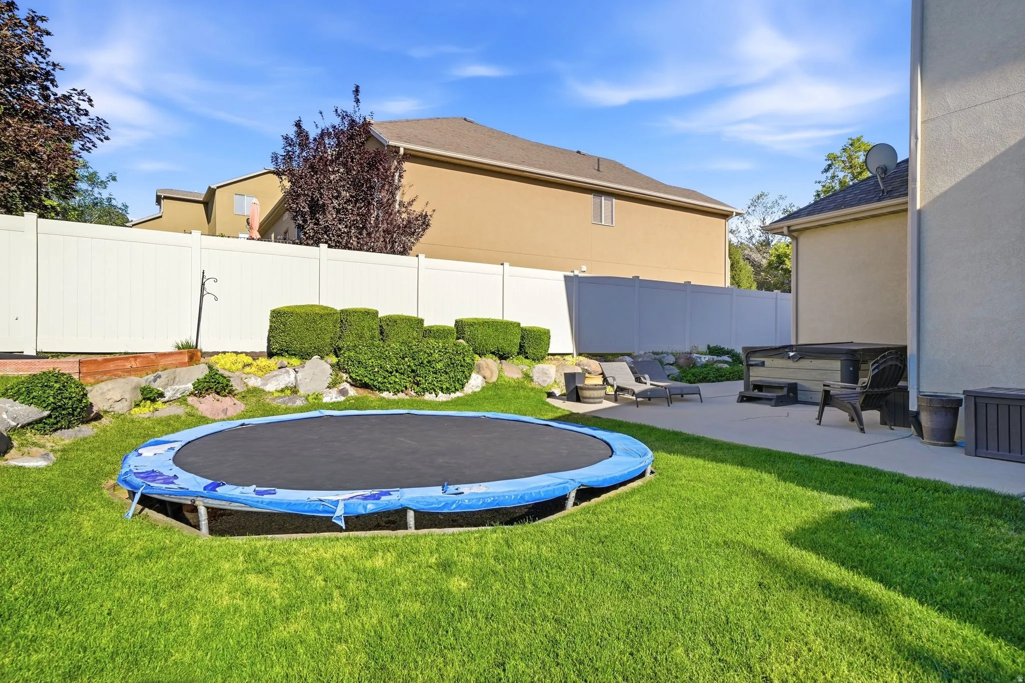 Expansive backyard featuring a large concrete patio, terraced landscaping, a white privacy fence and trampoline
