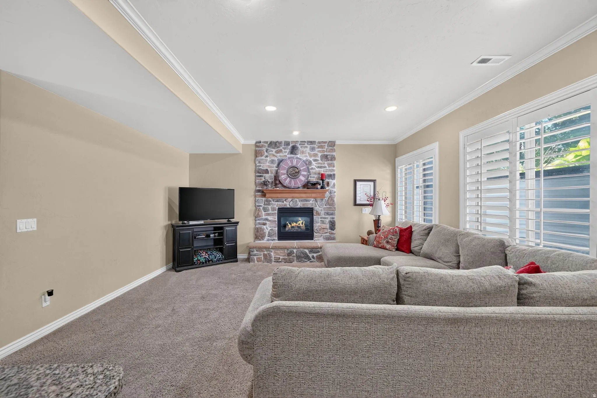 Basement living area featuring a stone-clad fireplace with a wood mantel, soft beige walls, and recessed lighting