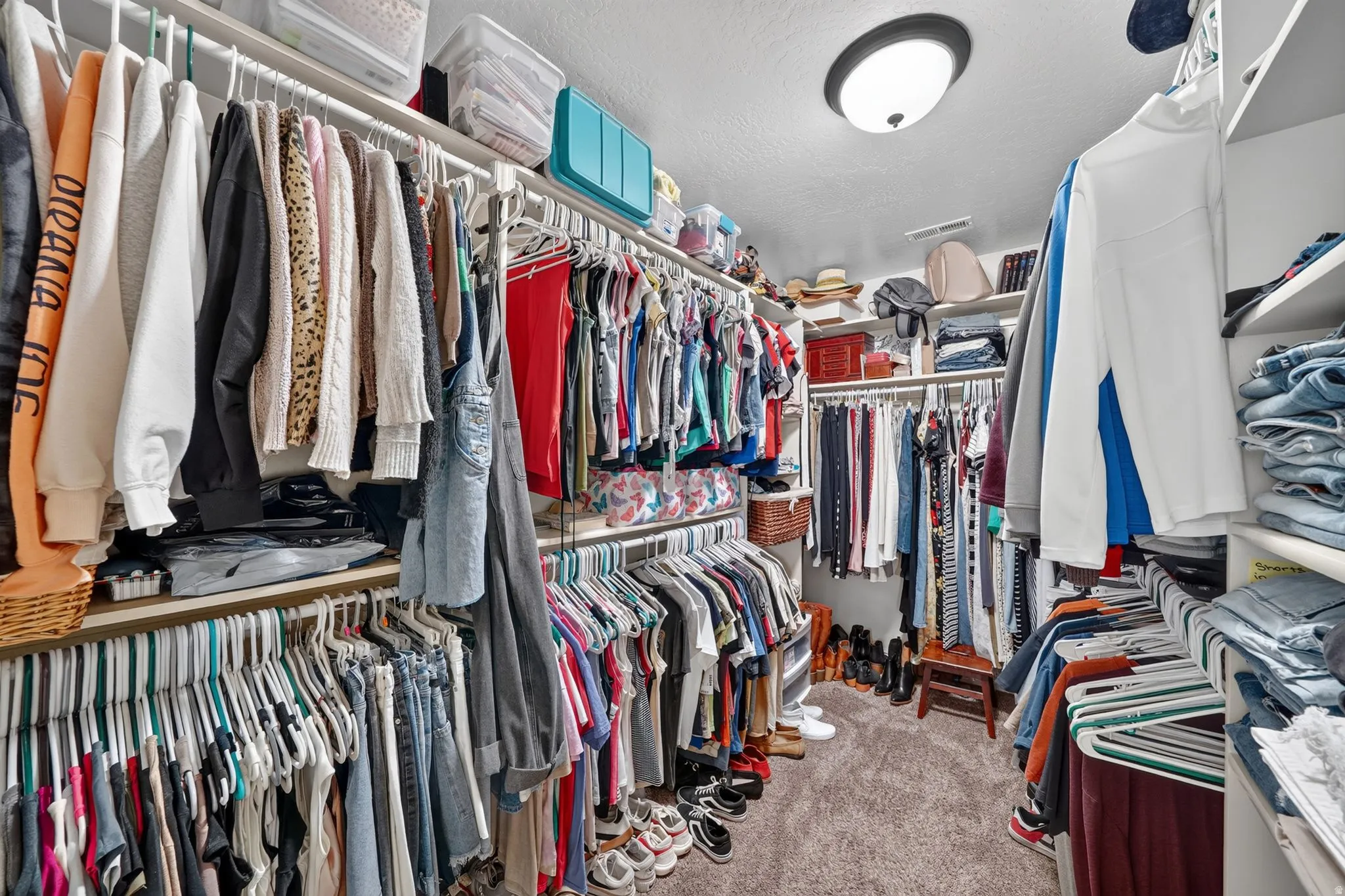 Spacious primary walk-in closet featuring extensive built-in shelving, multiple hanging rods, and recessed ceiling lighting