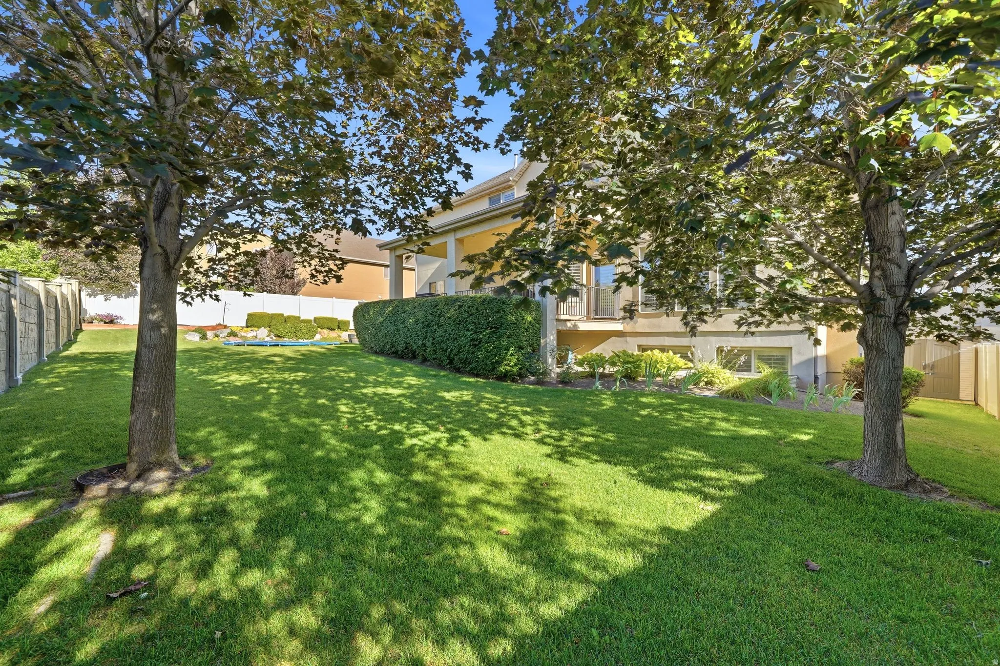 Expansive green lawn framed by mature trees, featuring a concrete perimeter fence and a manicured hedge row