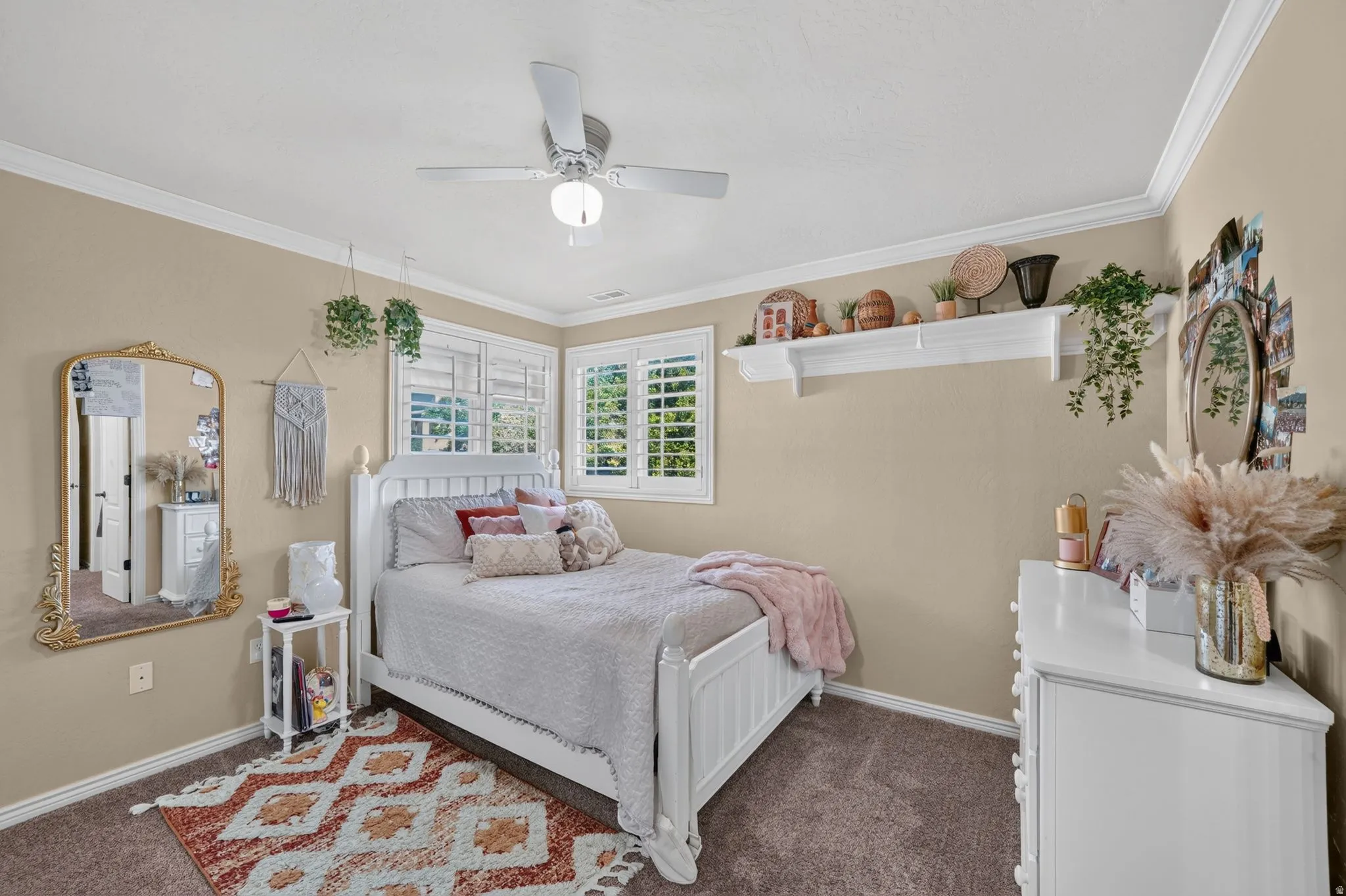 Spare bedroom featuring a white ceiling fan, crown molding, and two windows with white plantation shutters