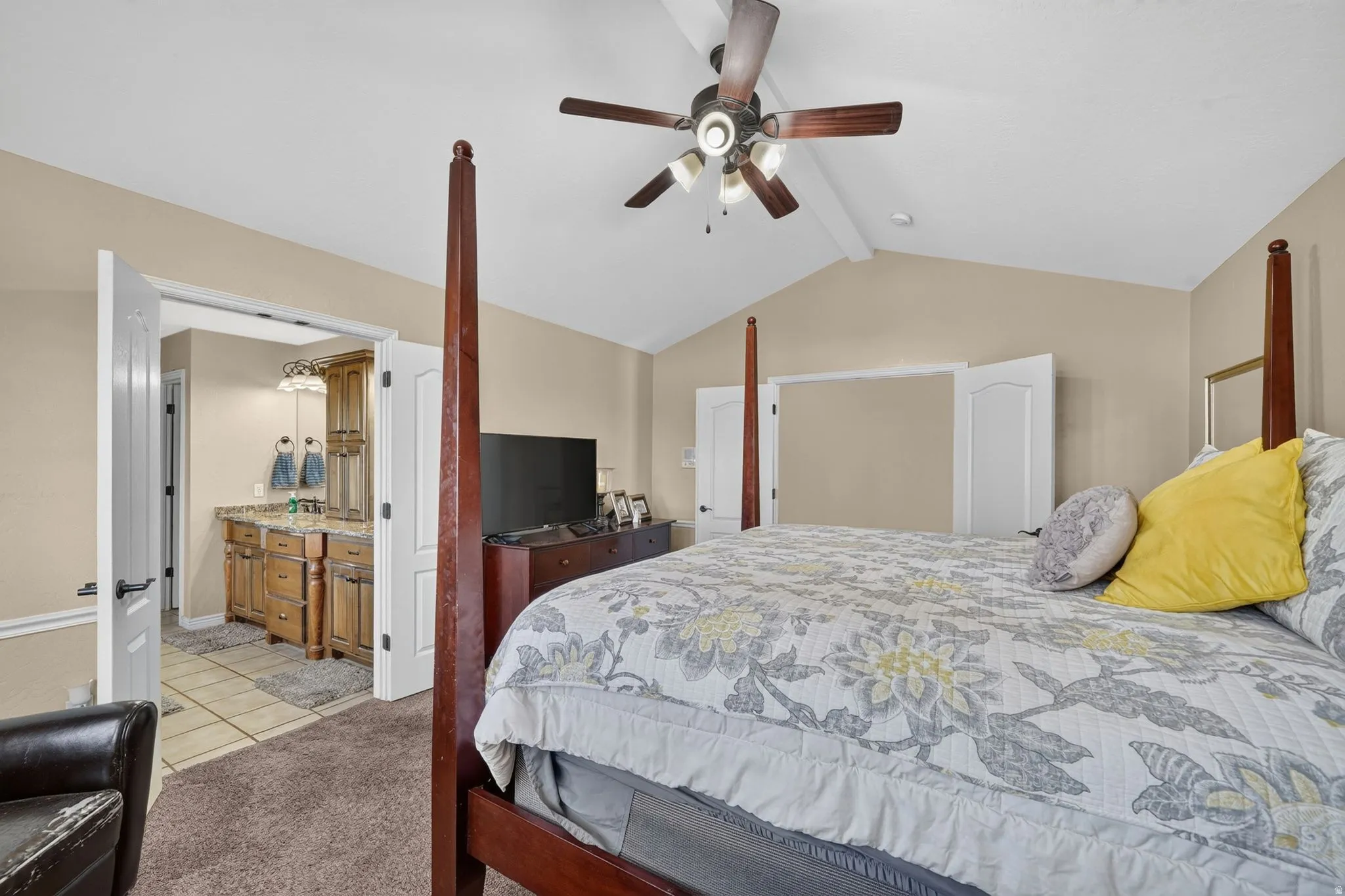 Large primary bedroom with vaulted ceiling with an exposed beam and ceiling fan