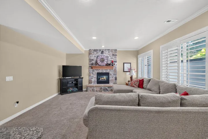 Basement living area featuring a stone-clad fireplace with a wood mantel, soft beige walls, and recessed lighting