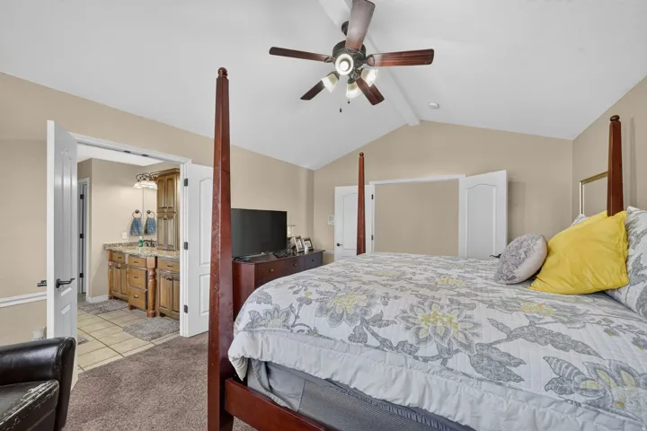 Large primary bedroom with vaulted ceiling with an exposed beam and ceiling fan