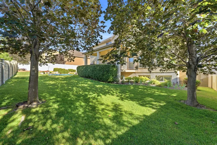 Expansive green lawn framed by mature trees, featuring a concrete perimeter fence and a manicured hedge row