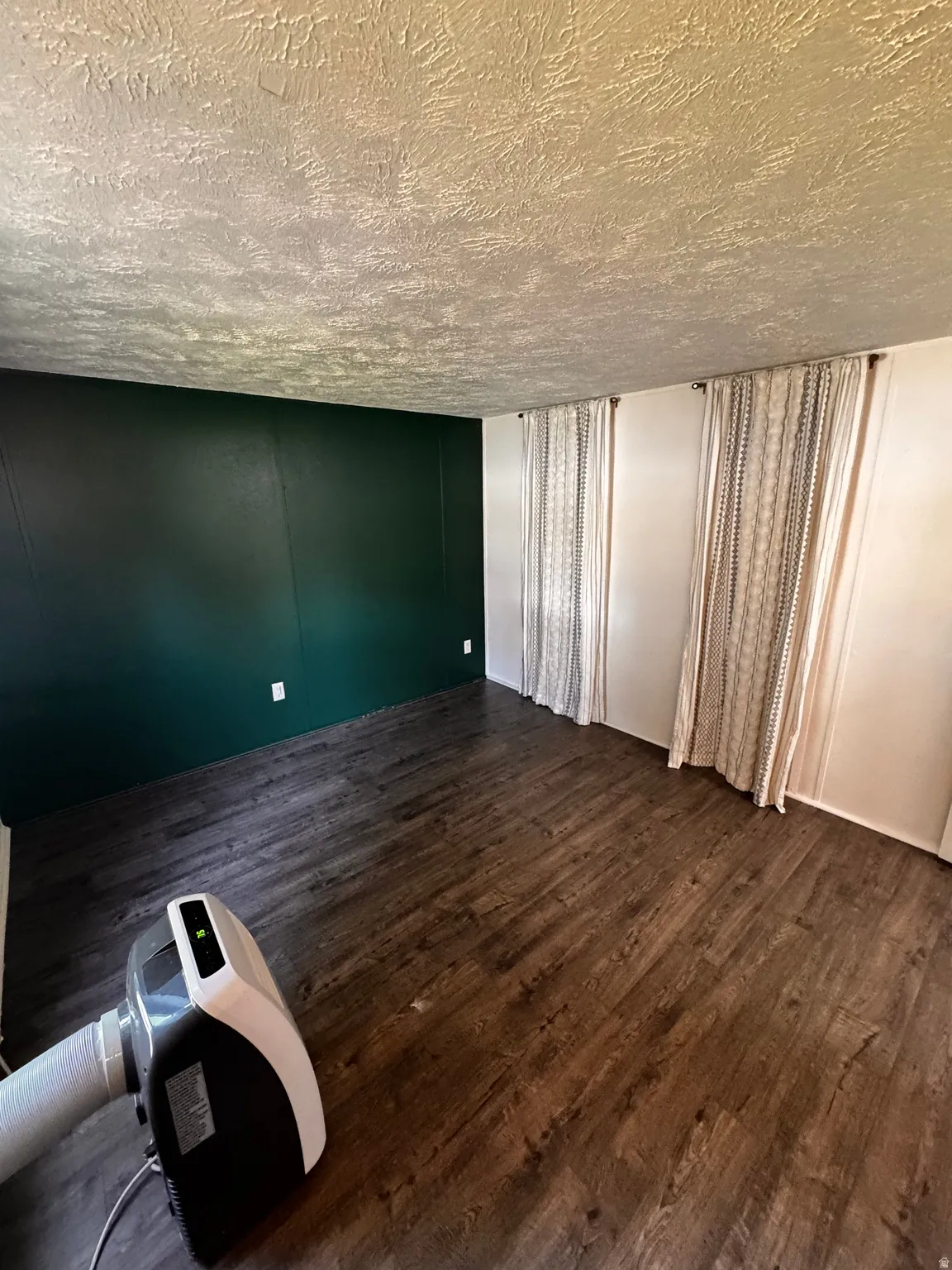 Room featuring dark wood-finish flooring, a painted accent wall, and two window openings
