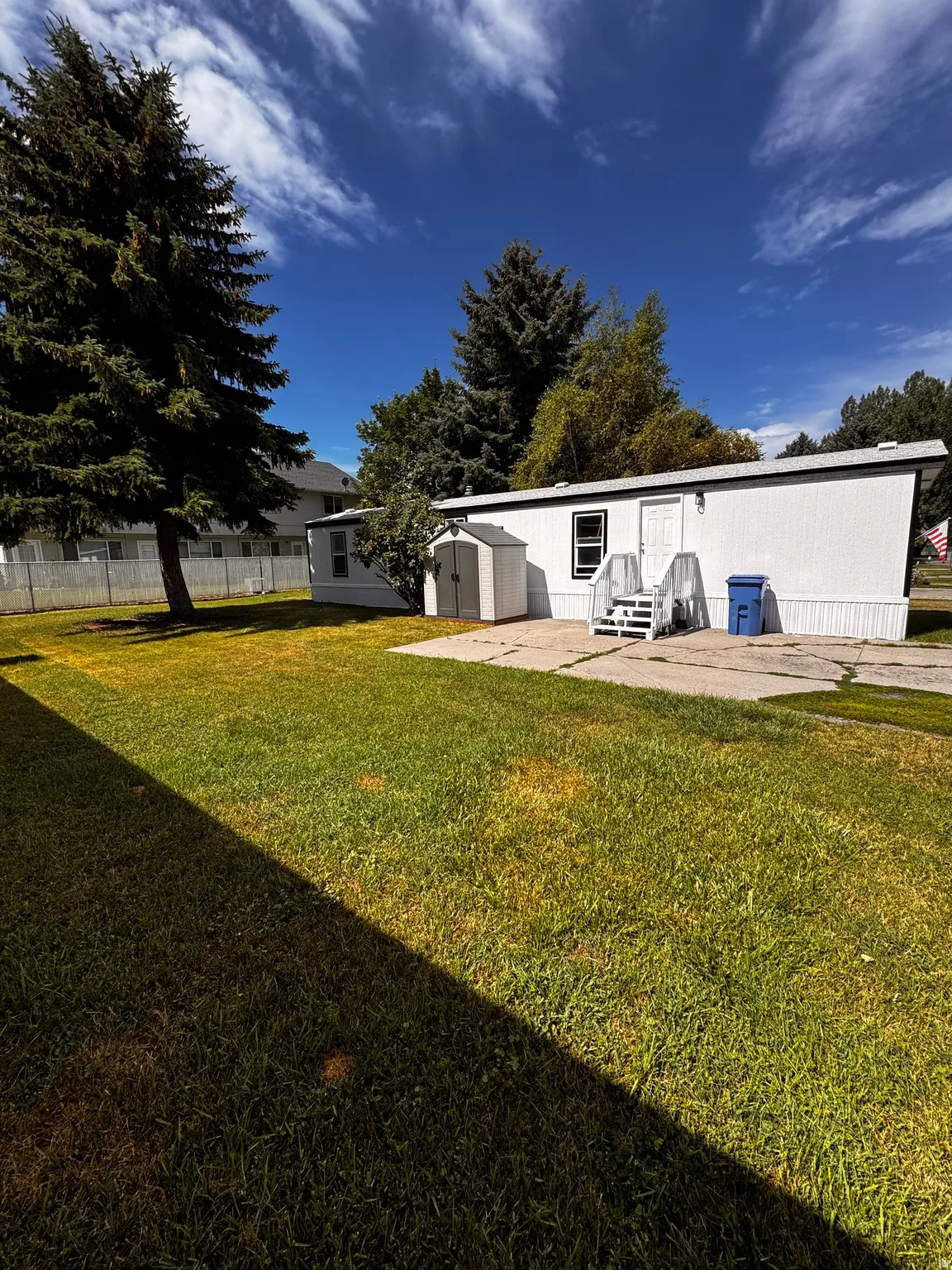Manicured lawn with a concrete patio, exterior shed, and mature trees