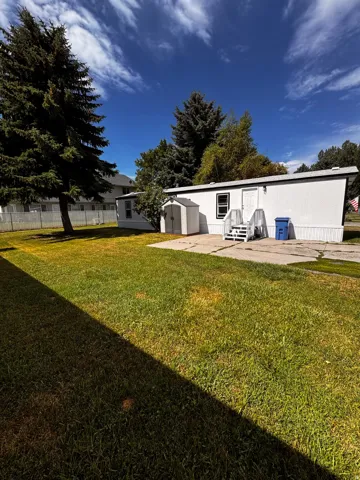 Manicured lawn with a concrete patio, exterior shed, and mature trees