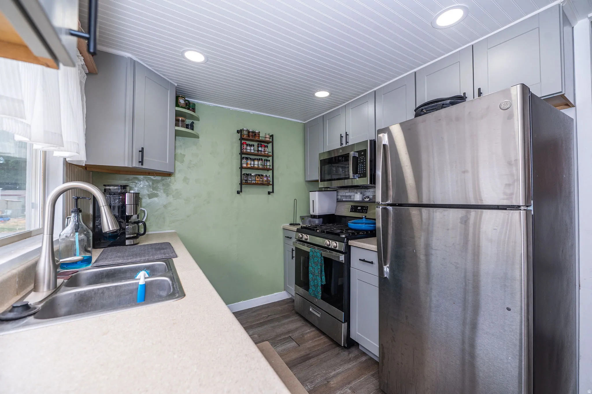 Well-equipped kitchen featuring stainless steel appliances, grey cabinetry, a stainless steel sink with a high-arc faucet, recessed lighting, and wood-finish flooring