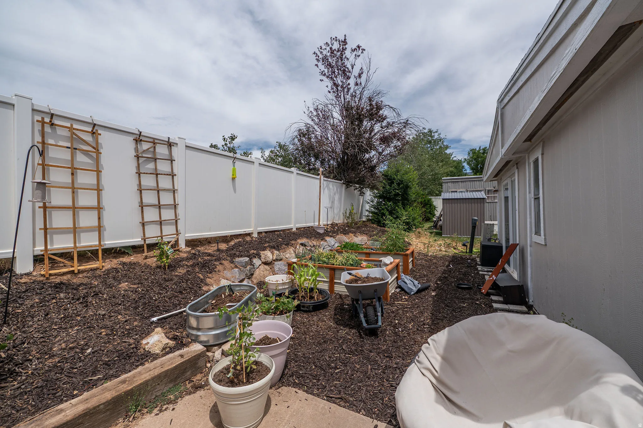Landscaped backyard featuring a white vinyl privacy fence, a raised garden bed, and a detached storage shed