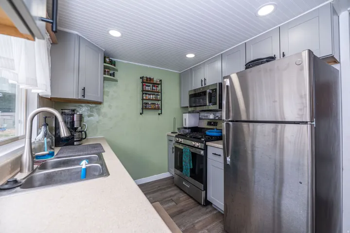 Well-equipped kitchen featuring stainless steel appliances, grey cabinetry, a stainless steel sink with a high-arc faucet, recessed lighting, and wood-finish flooring
