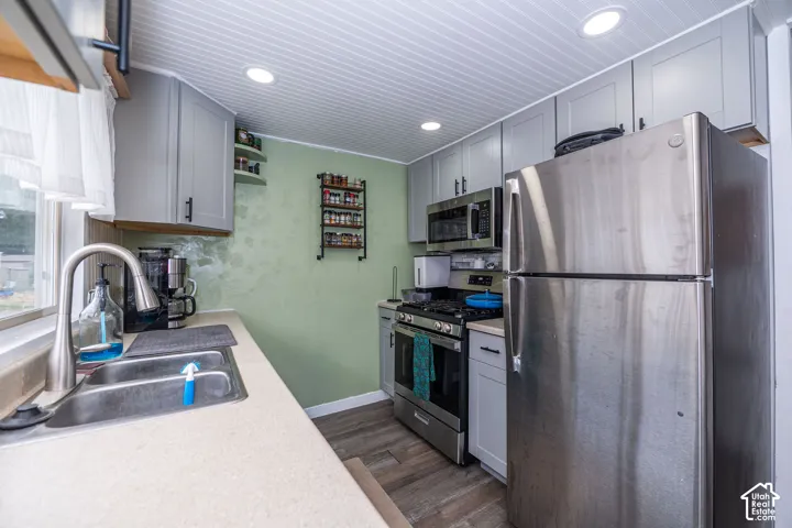 Well-equipped kitchen featuring stainless steel appliances, grey cabinetry, a stainless steel sink with a high-arc faucet, recessed lighting, and wood-finish flooring