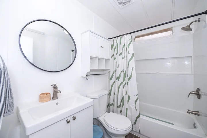 Bathroom featuring a white vanity with integrated sink, brushed nickel faucet, and circular black-framed mirror