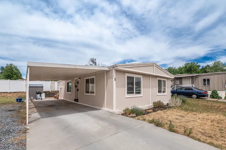 Exterior featuring beige siding with white trim, a covered carport, a concrete driveway, and a white privacy fence