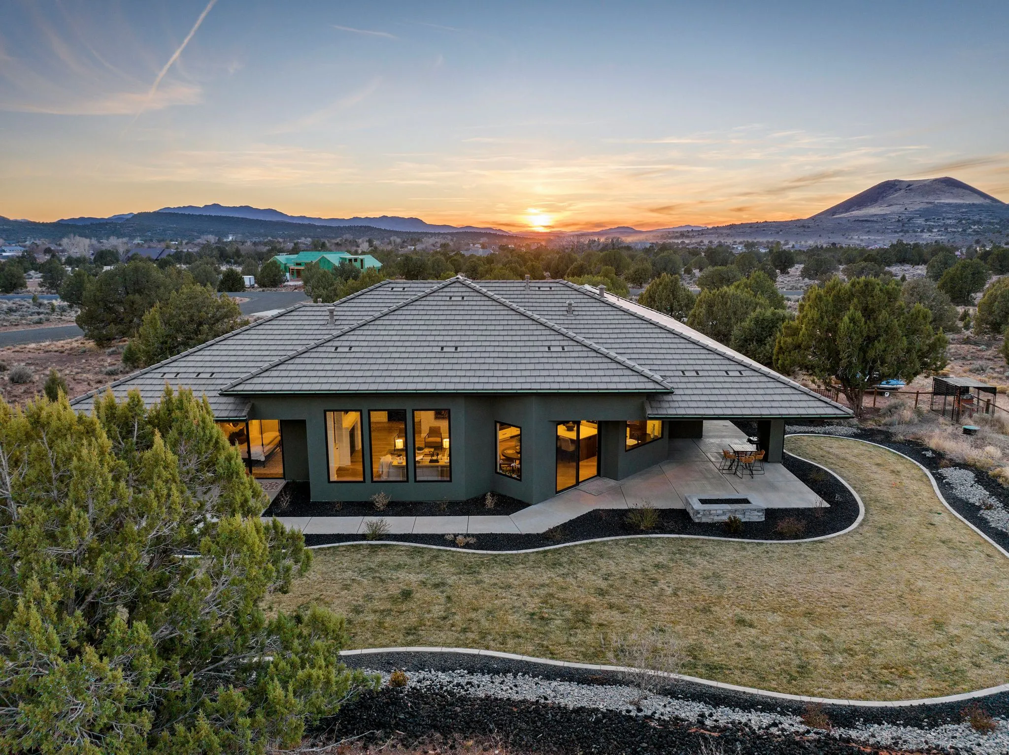 Modern single-story residence with a multi-paneled tile roof, featuring an expansive concrete patio, built-in fire pit, and low-maintenance landscaping with decorative rock beds