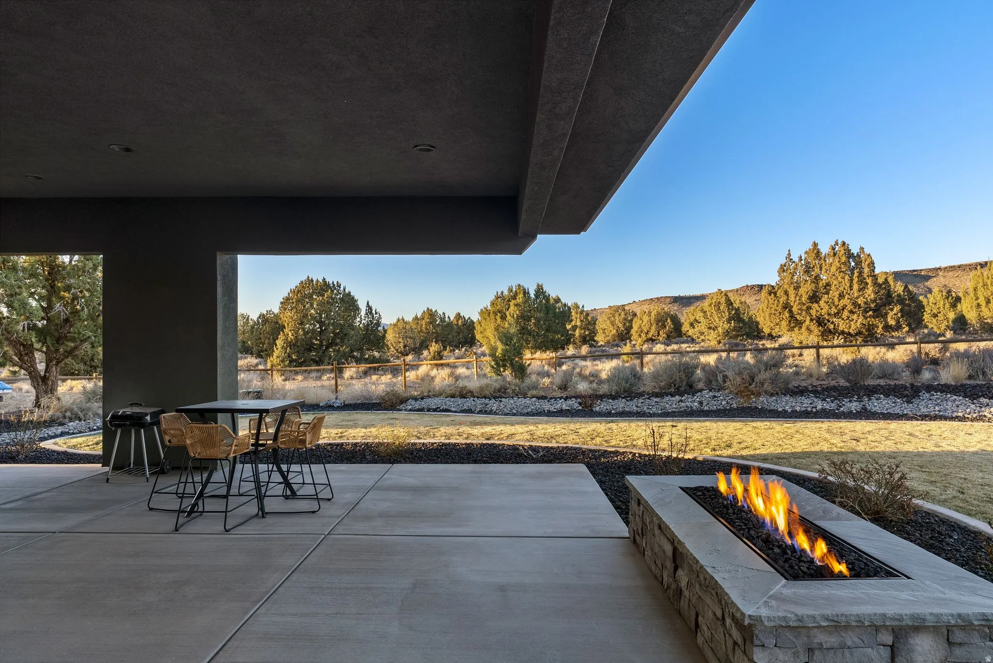 Expansive outdoor patio featuring a stone-clad fire pit, concrete pavers, and an overhead structural overhang