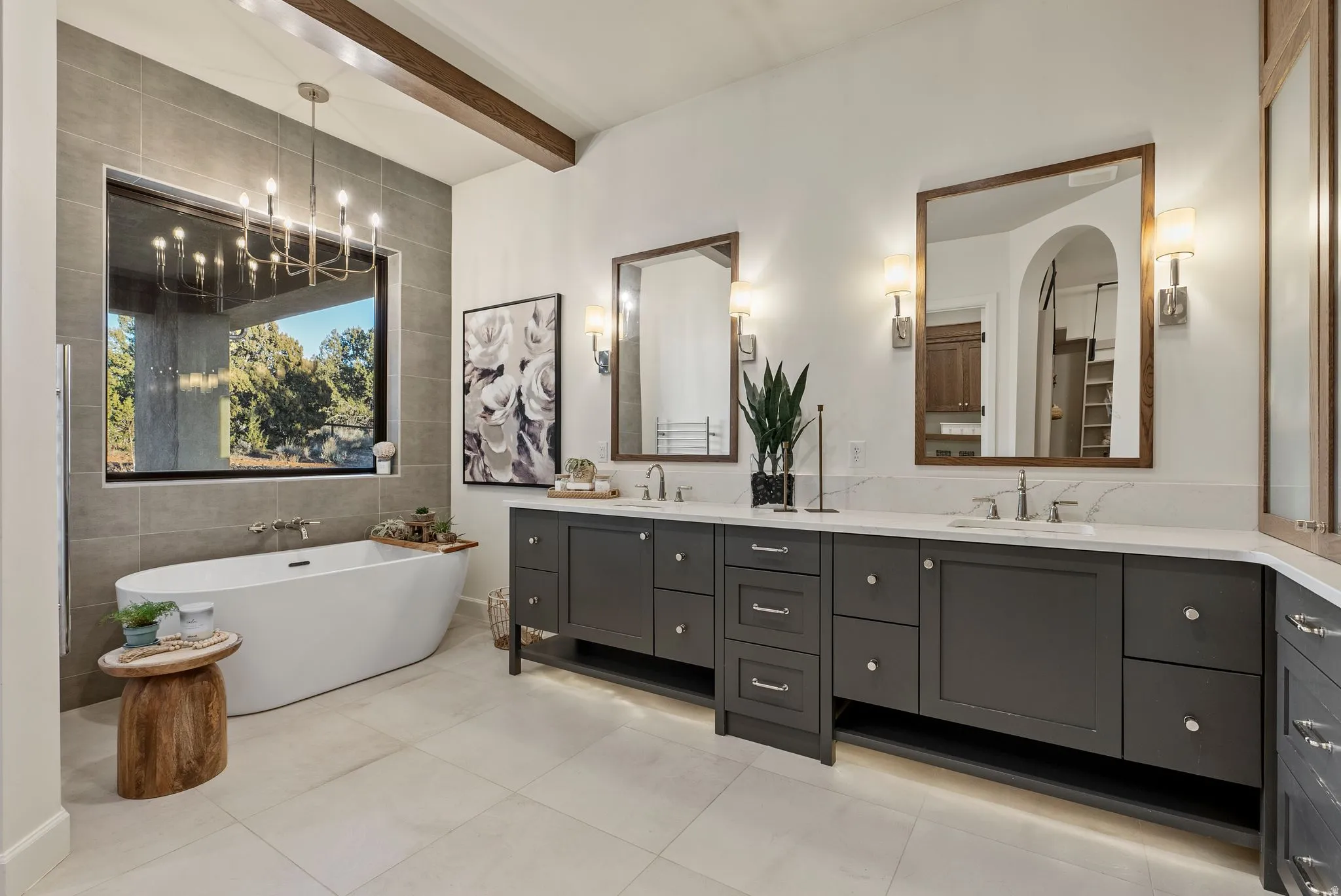 Freestanding soaking tub with a large window surround, dual dark wood-finish vanities with light countertops, individual wall-mounted mirrors, and recessed lighting
