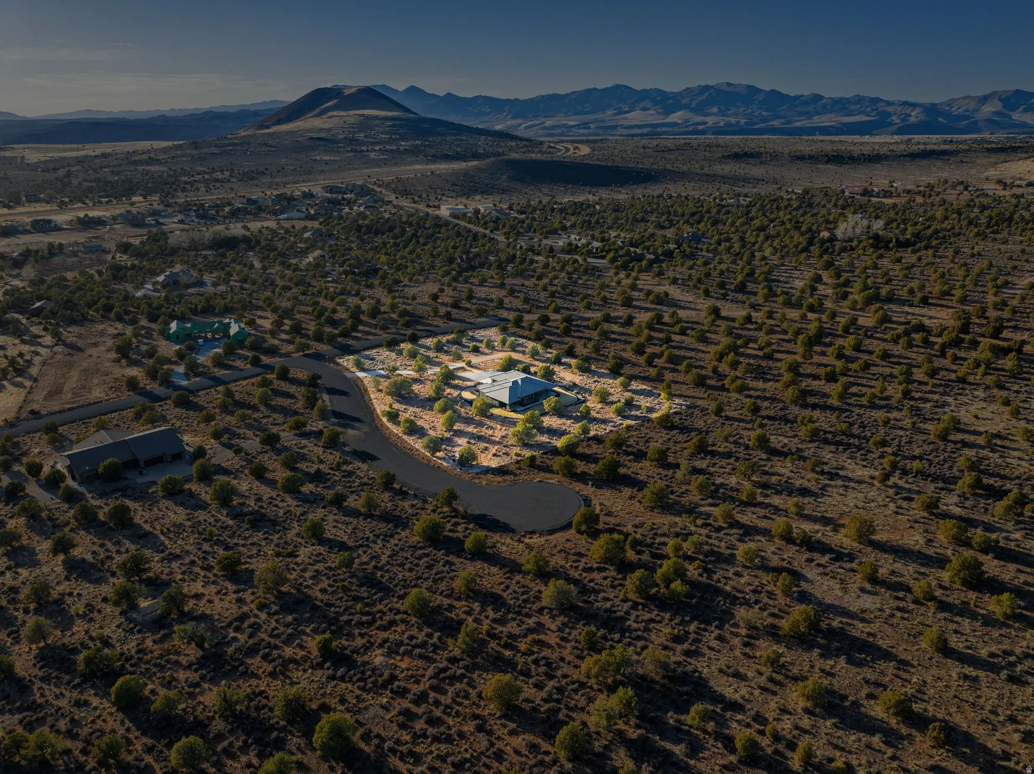 Expansive desert landscape featuring a paved residential road and distant mountain ranges