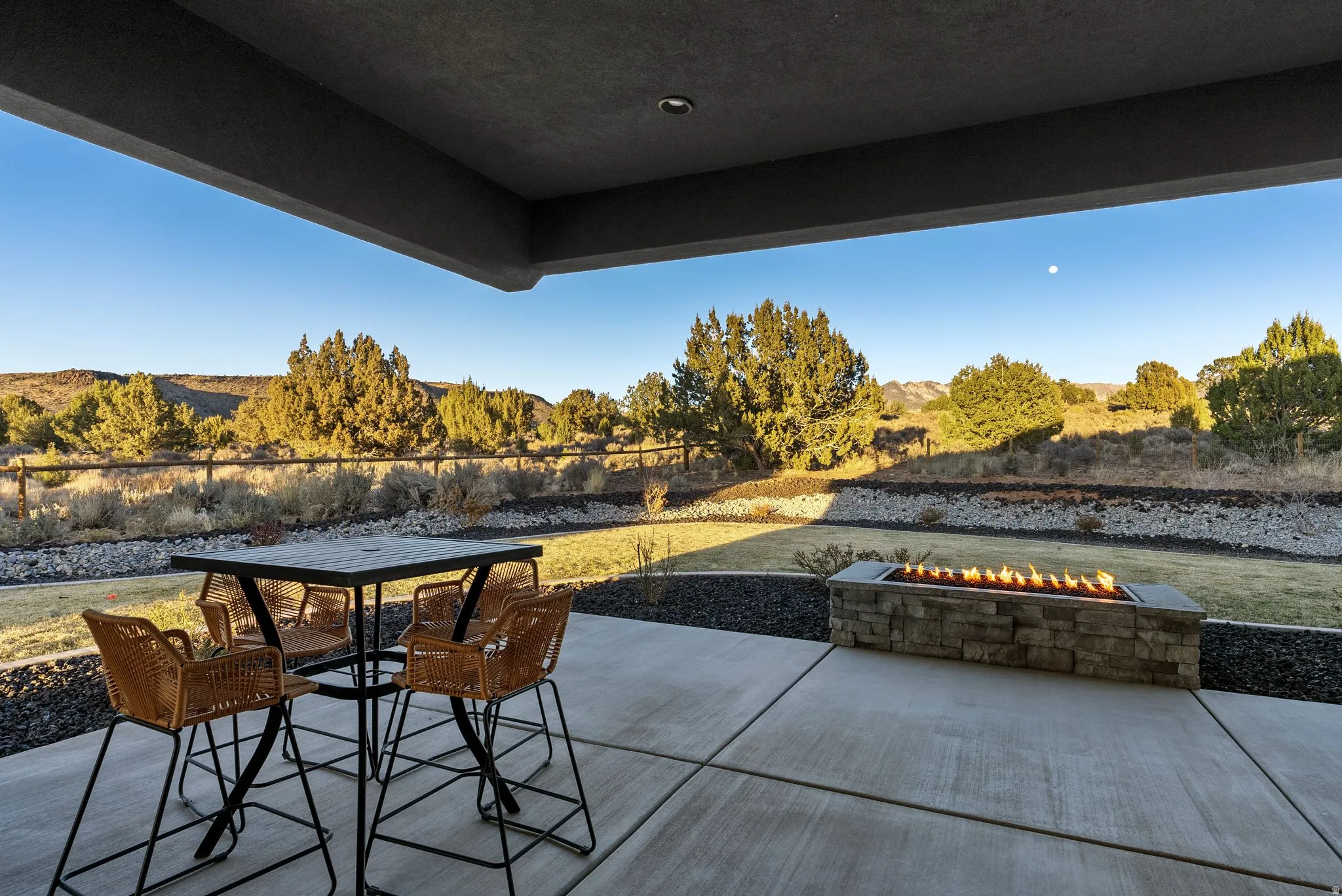 Expansive covered patio featuring a stone-clad fire pit, concrete pavers, and a distant natural landscape
