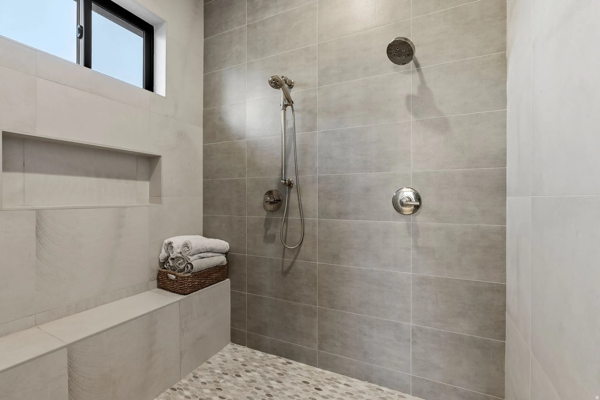Shower featuring a built-in bench, recessed shelf, and pebble-finish floor