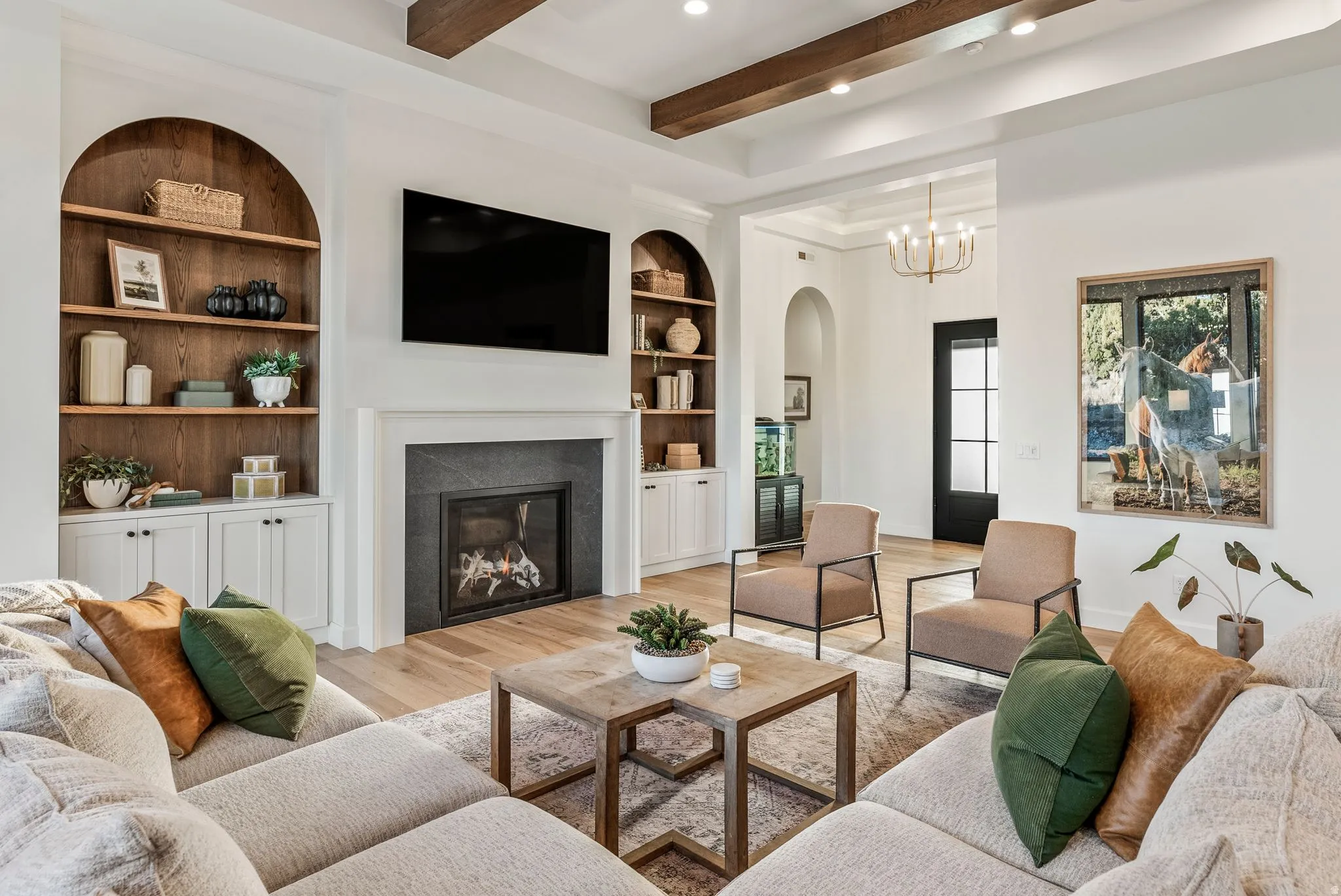 Spacious living area featuring exposed wood beams, wood-finish flooring, a contemporary fireplace with a dark stone surround, and built-in arched shelving with lower cabinetry