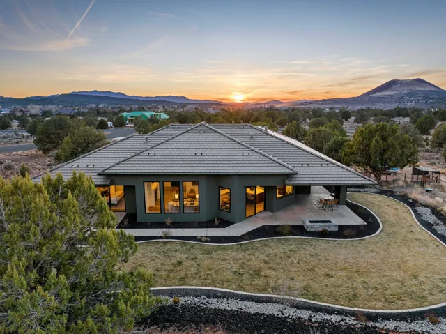 Modern single-story residence with a multi-paneled tile roof, featuring an expansive concrete patio, built-in fire pit, and low-maintenance landscaping with decorative rock beds