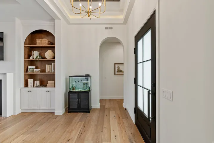 Entryway featuring a dark-framed full-light door with frosted panels, light wood-finish flooring, a coffered ceiling with a gold-tone chandelier, and an arched built-in bookshelf with lower cabinetry