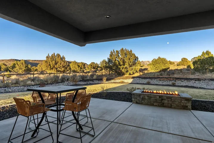 Expansive covered patio featuring a stone-clad fire pit, concrete pavers, and a distant natural landscape