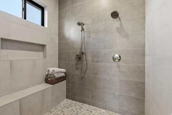 Shower featuring a built-in bench, recessed shelf, and pebble-finish floor