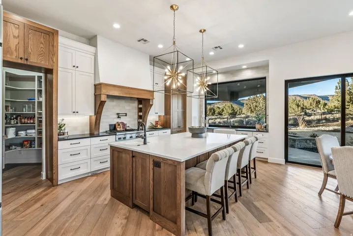 Gourmet kitchen with a large central island, white cabinetry, integrated range hood, and a walk-in pantry