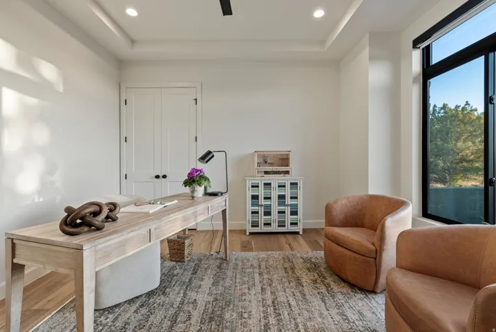 Bright interior room featuring a tray ceiling with recessed lighting, double panel doors, wood-finish flooring, and a large window with black trim