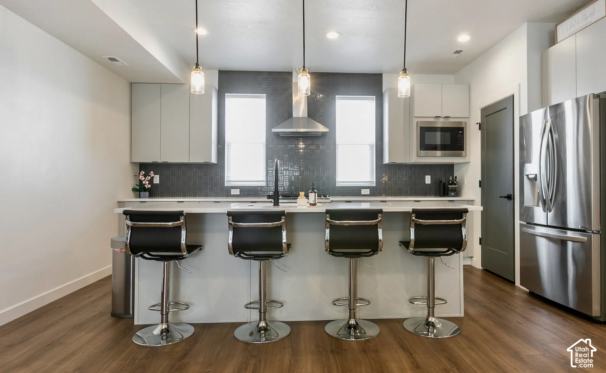 Contemporary kitchen featuring a large island with quartz countertop, stainless steel appliances, upper cabinetry, and wood-finish flooring