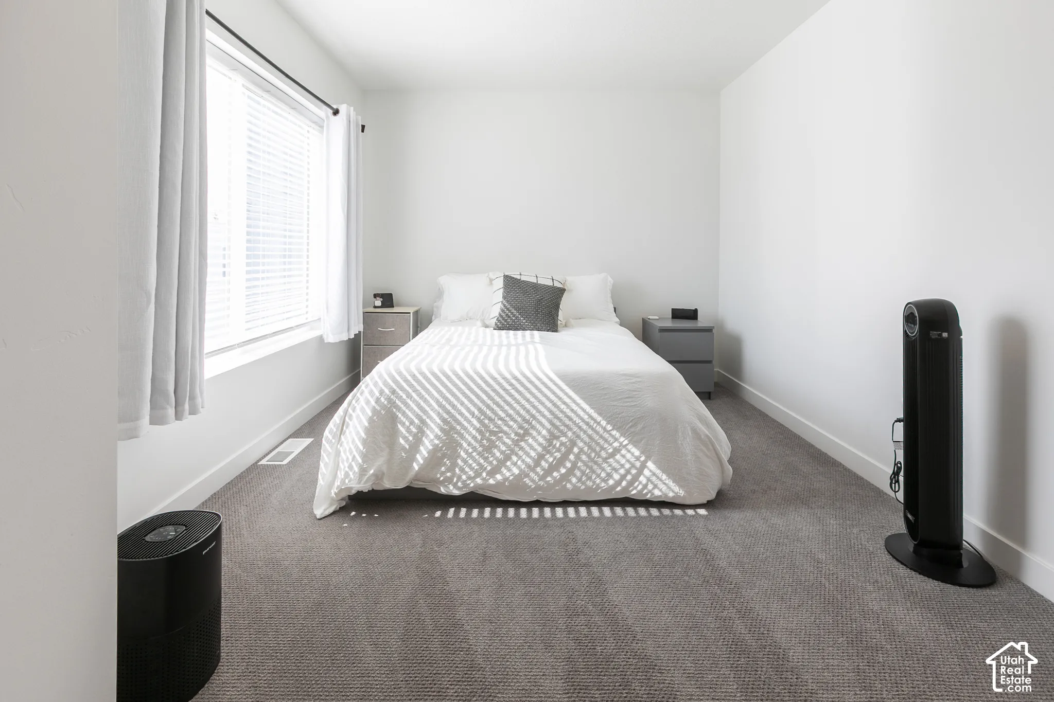 Bedroom featuring neutral-toned carpet, white walls, and a large window with blinds