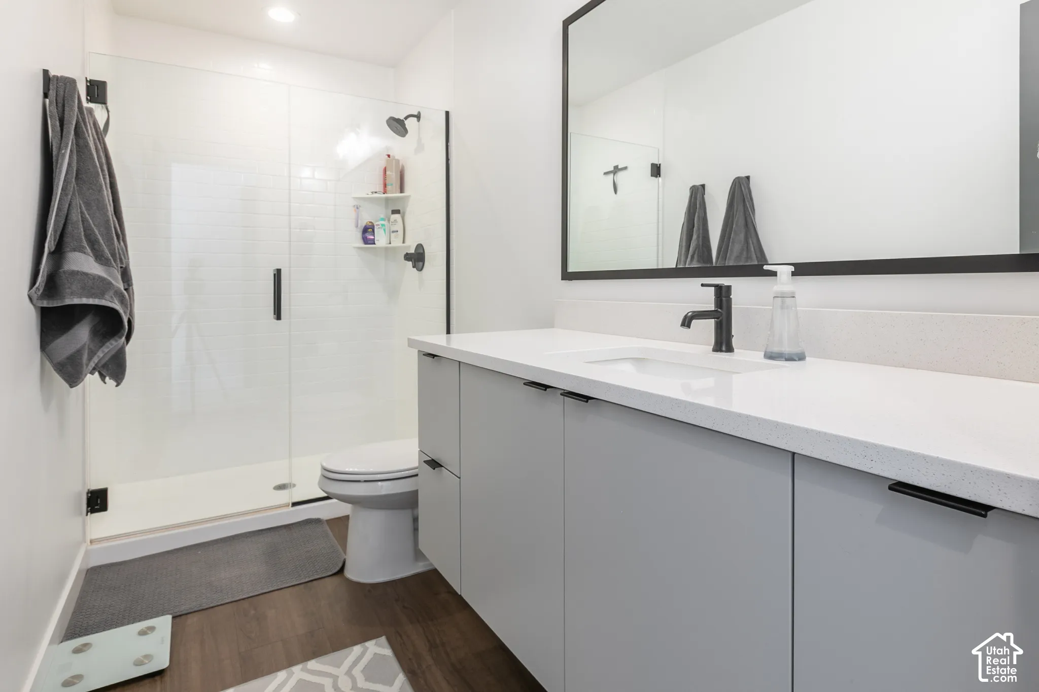 Contemporary bathroom featuring a spacious glass-enclosed shower with white subway tile, a wide vanity with light gray cabinetry, a white countertop, and a large framed mirror